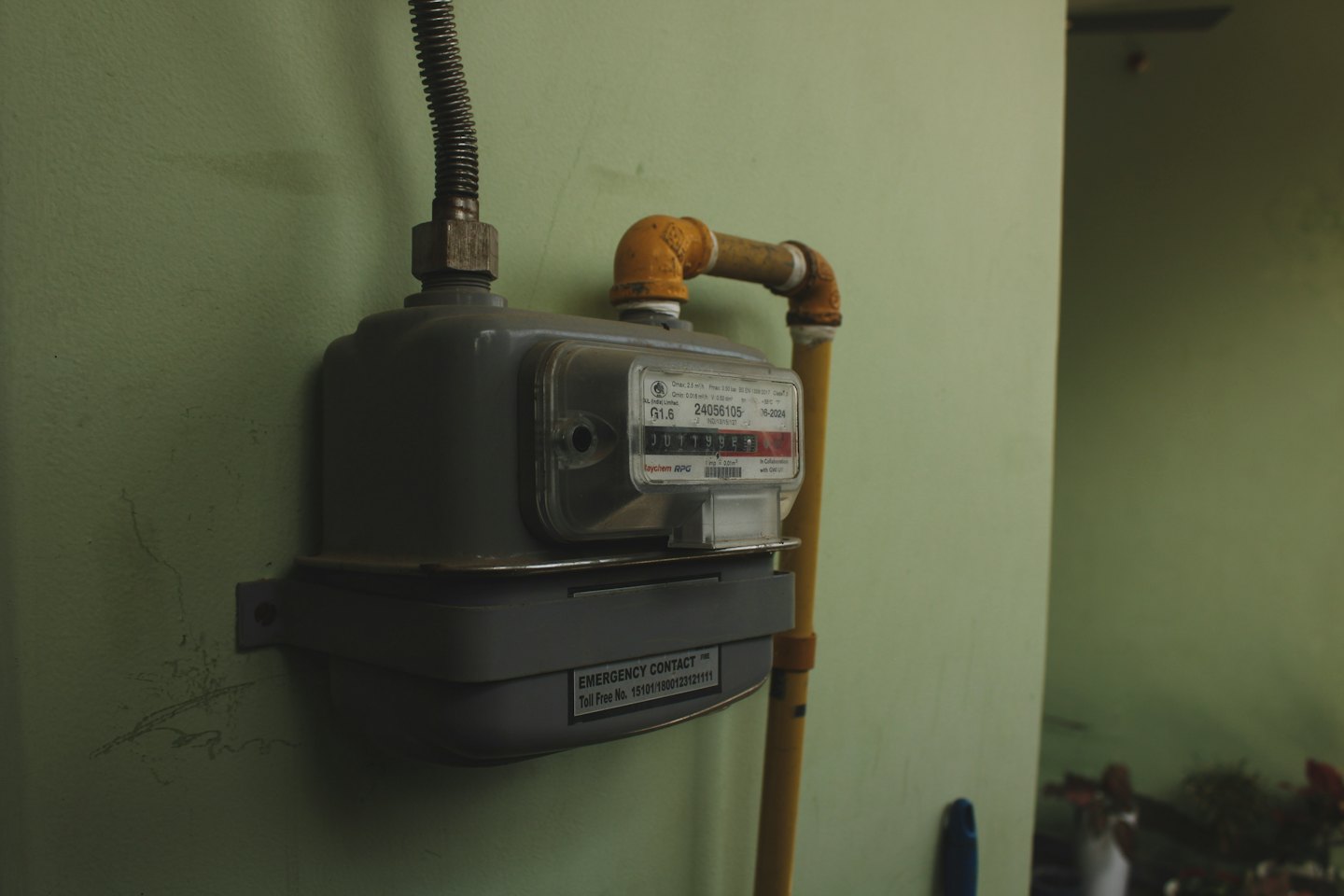 Gray domestic gas meter mounted on a green wall.